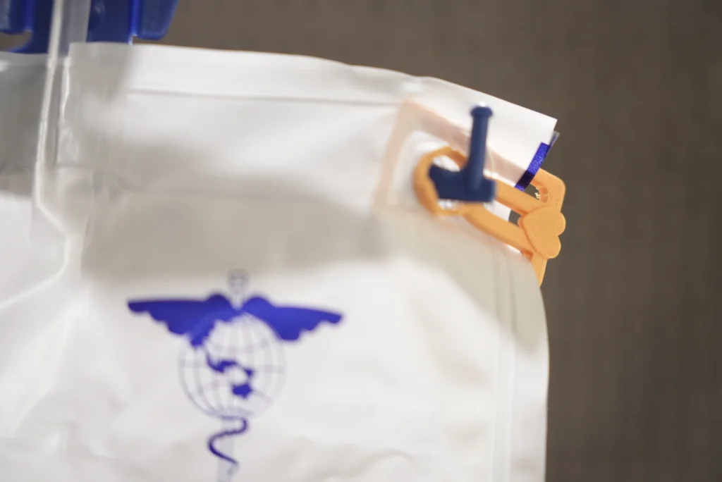 Close view of a Uroclip fitted over the hanging hole of a demonstrated compatible urine bag